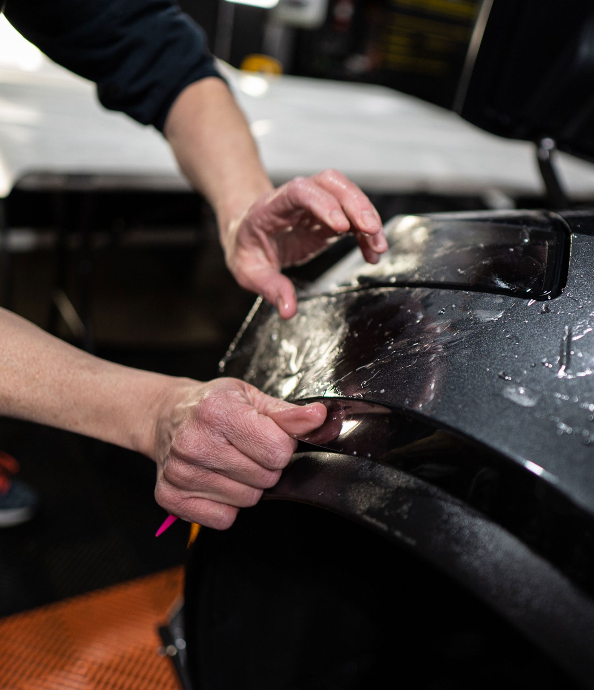 A close up of a person applying a protective film to a car fender