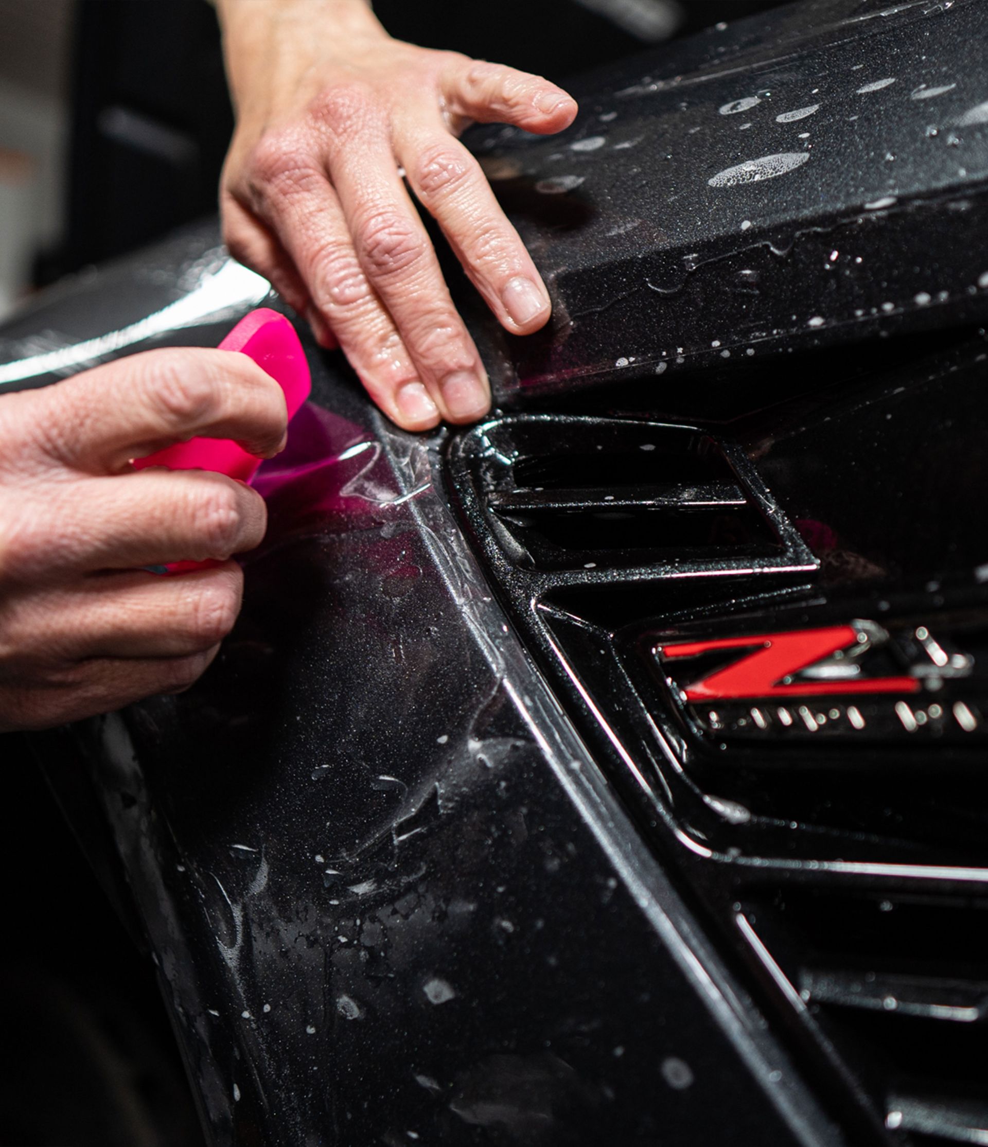 A person is applying a ppf to the front of a car.