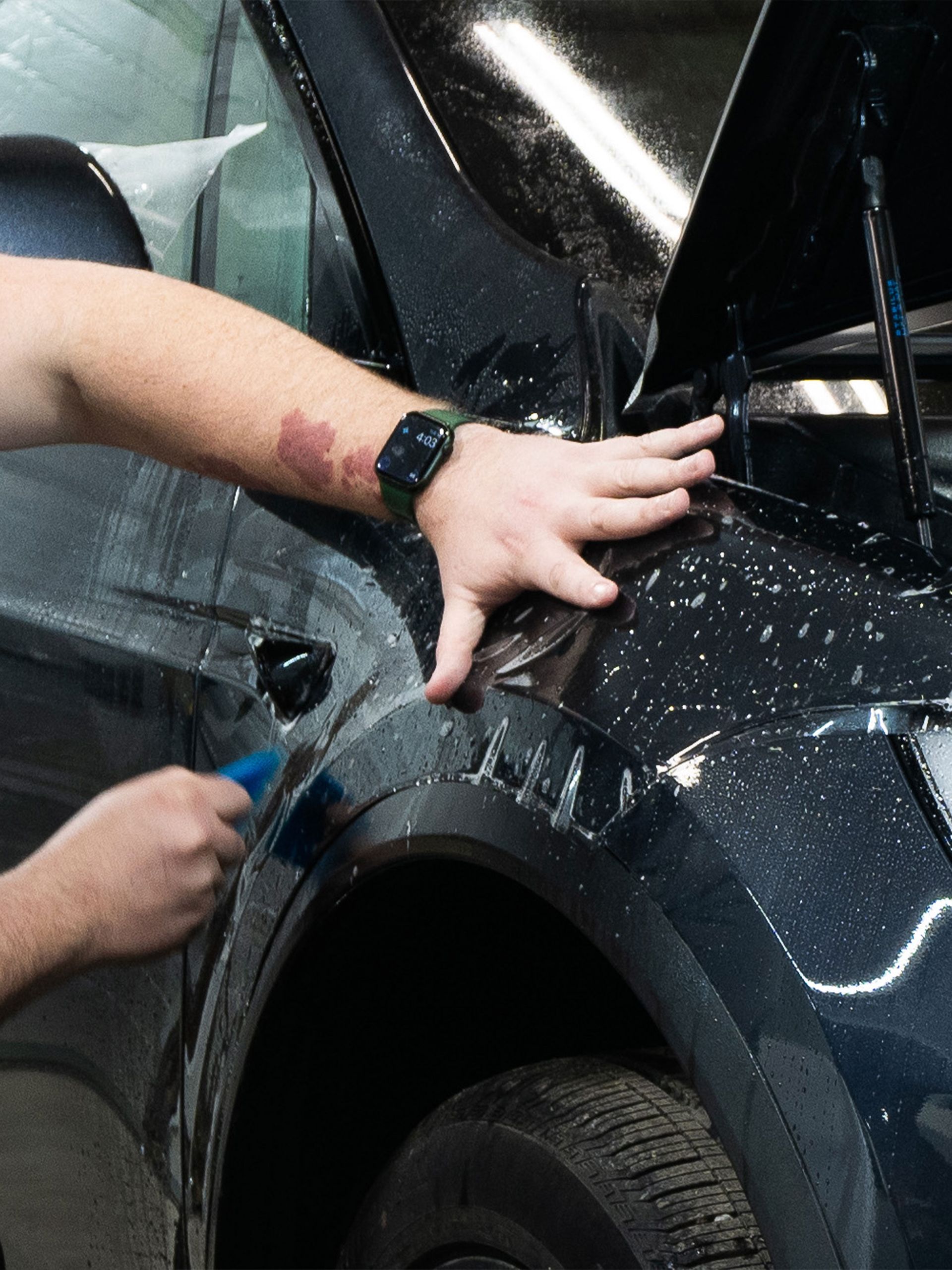 A man is cleaning the side of a car with a brush.