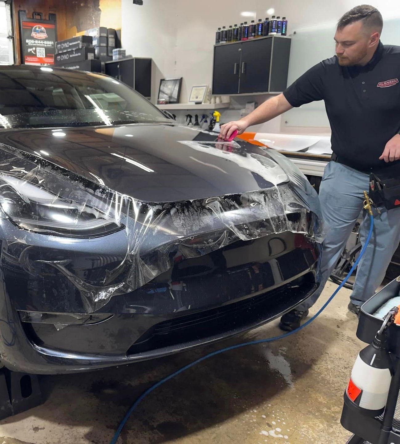 A man is wrapping a car with plastic wrap in a garage.