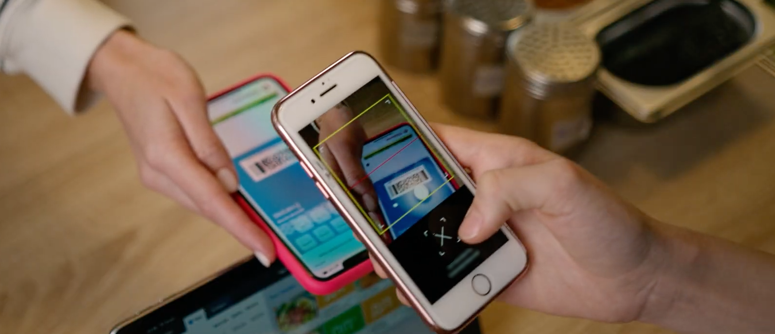 Two hands holding smartphones over a table, showing app screens with colorful displays