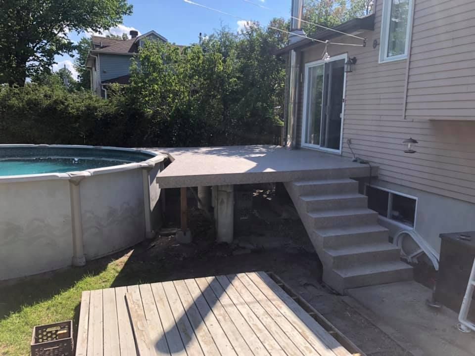 Une terrasse avec des escaliers menant à une piscine à côté d'une maison.