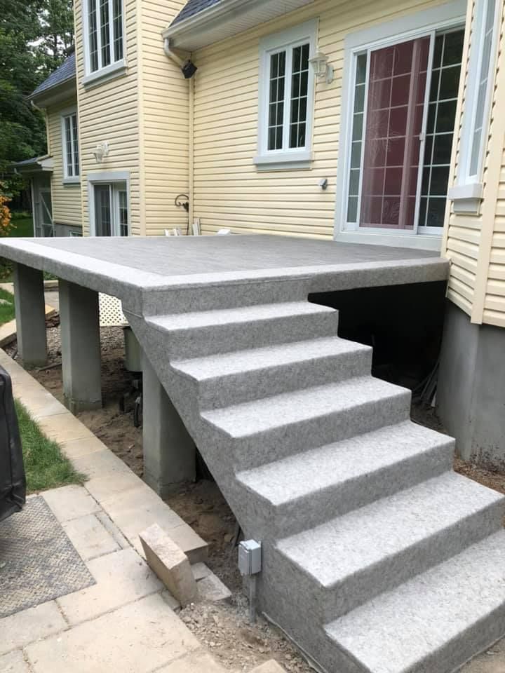 Une terrasse en membrane de pvc avec des escaliers qui y mènent devant une maison.