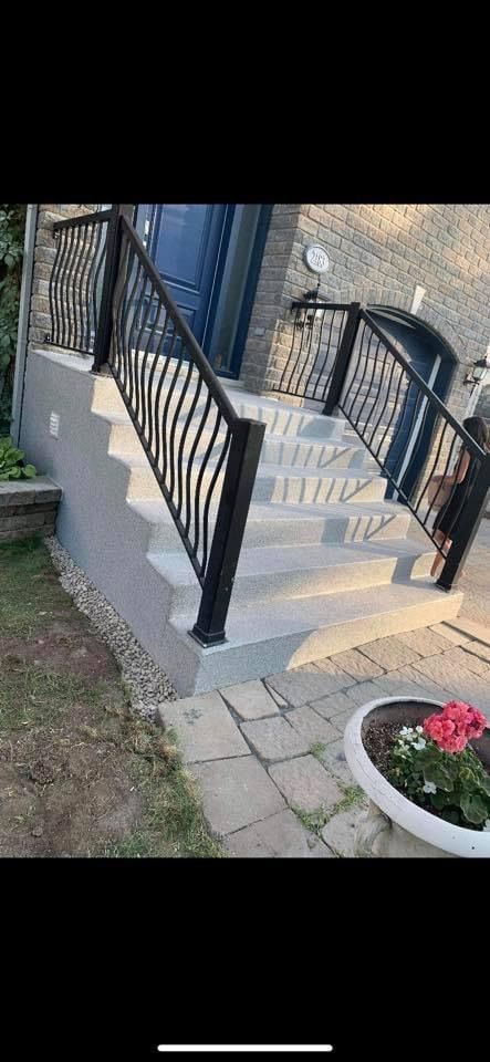 Un escalier recouvert de membrane de pvc menant à une maison avec une balustrade noire.
