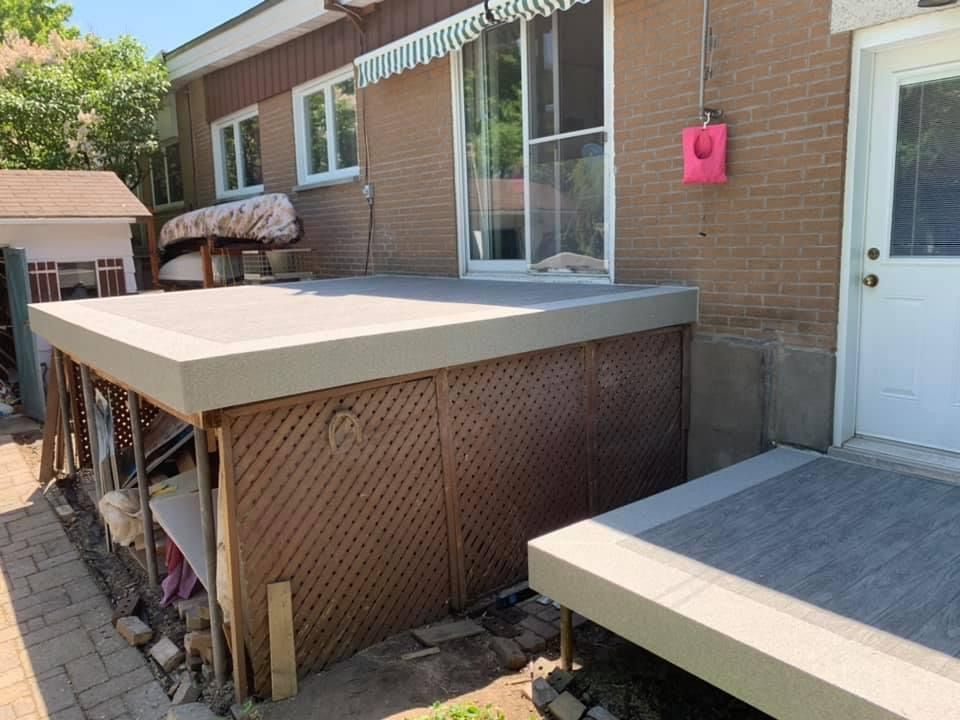 Une terrasse en membrane de pvc est en cours de construction sur le côté d'une maison en briques.