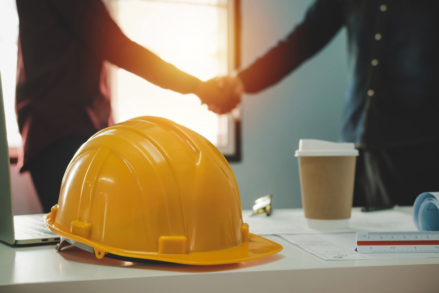 En client et un entrepreneur qui se serrent la main, avec un casque de construction et un café en pr
