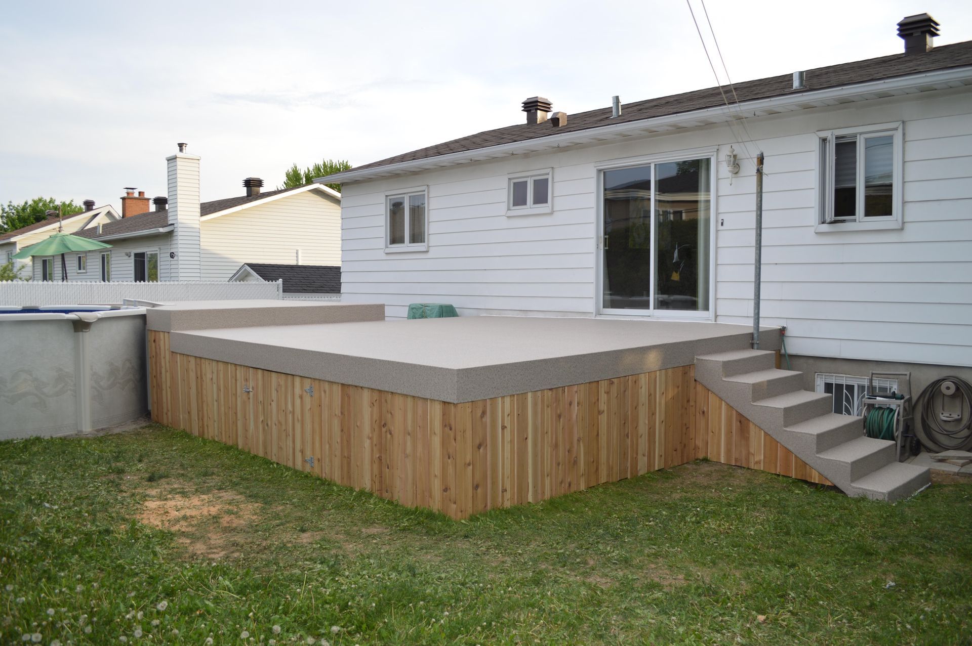 Une maison blanche avec une terrasse en bois recouverte de membrane de pvc et des escaliers devant.