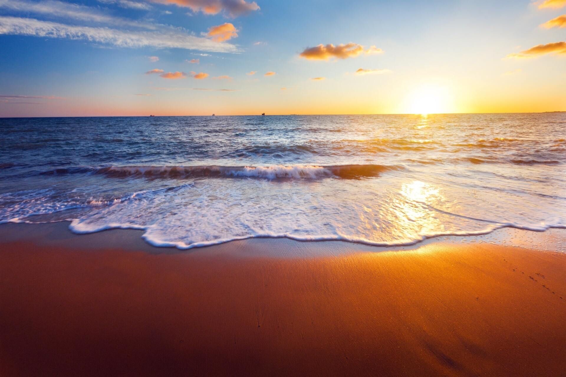 Sunset over a calm ocean with waves lapping a sandy beach and warm orange reflections