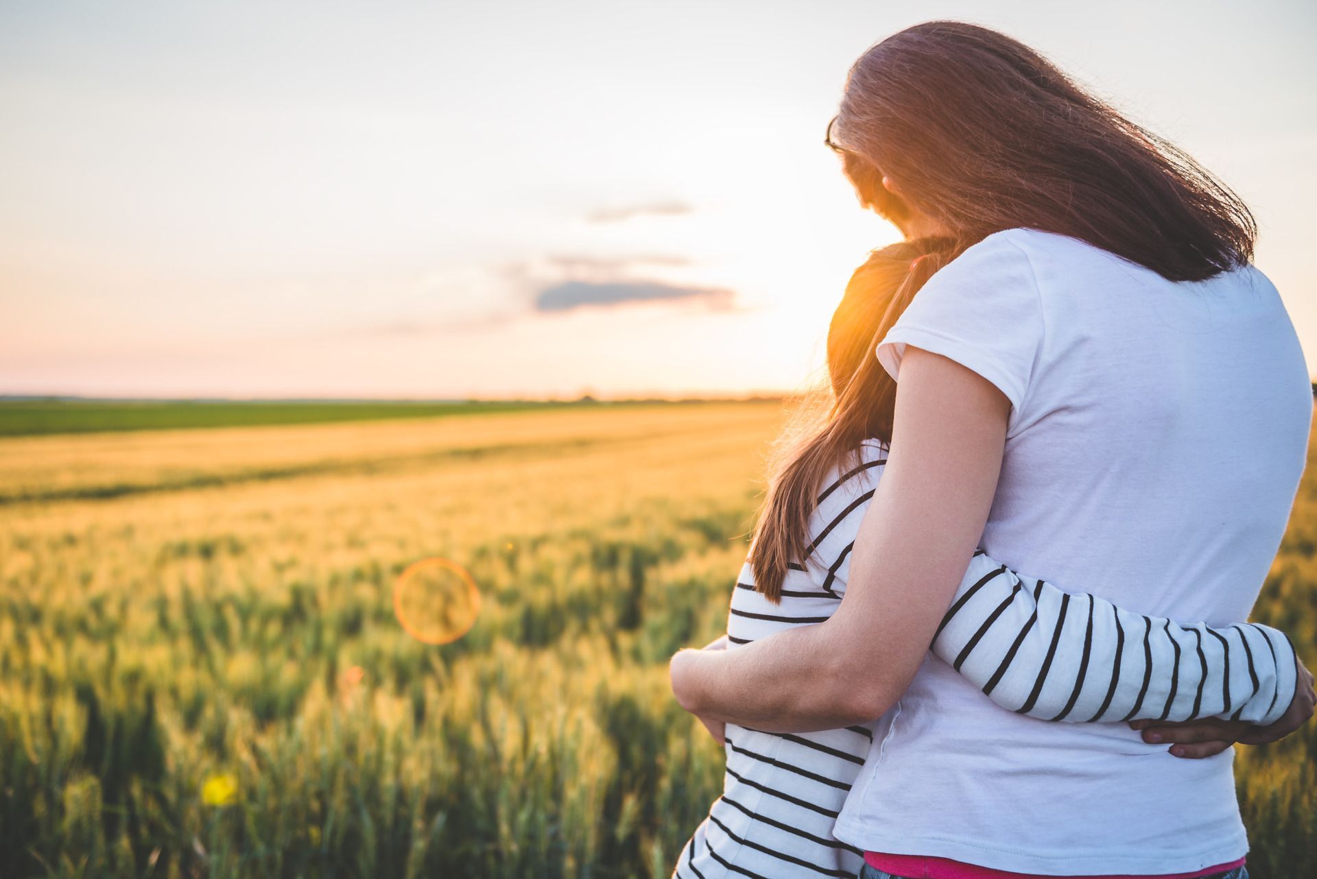 Woman embraces child in a wheat field at sunset.
