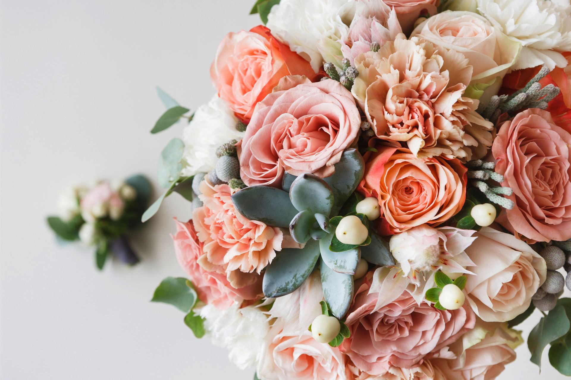 Bouquet of pink and peach roses with greenery and a boutonniere on a white surface.
