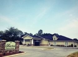 Barton Funeral Home building, beige with dark roof, sign with address in front, under a clear sky.