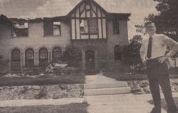A man in a suit and tie is standing in front of a large house.