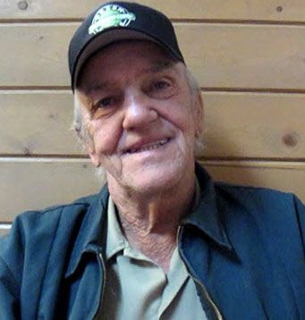 An older man wearing a hat and a jacket is smiling for the camera.