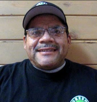 A man wearing glasses and a hat with the word green on his shirt