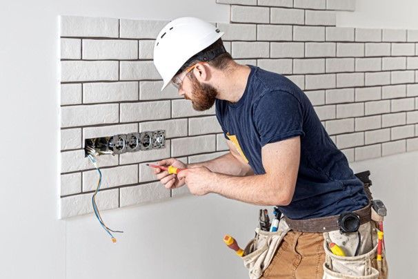 A man is working on an electrical outlet on a brick wall.