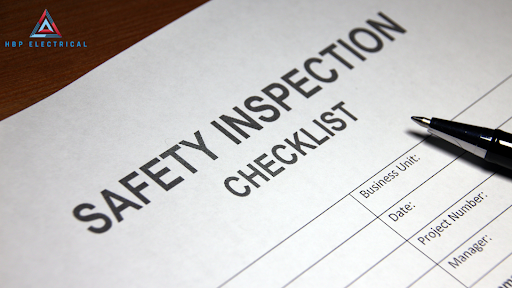 Two men are working on an electrical box. Safety inspection checklist with pen ready for documentation.