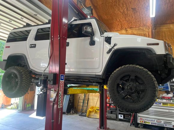 White Hummer SUV raised on a lift in a garage, showcasing the underside of the vehicle.