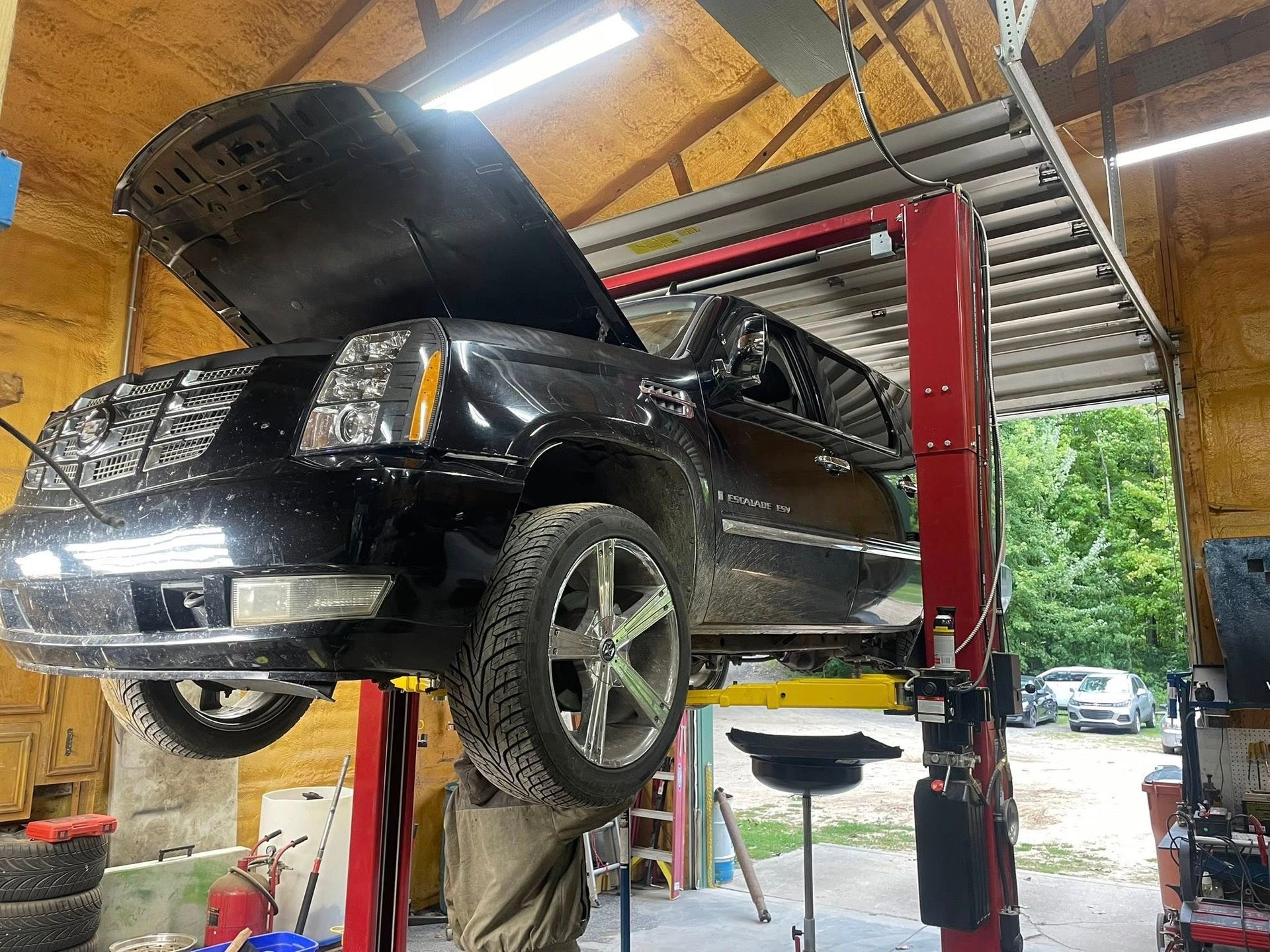 Black SUV on a hydraulic lift inside a garage, hood open.