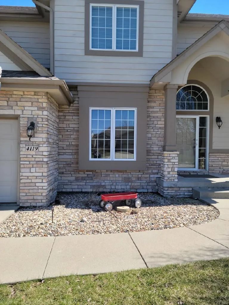Two-story house with stone veneer, white windows, and an arched front door. A red wagon sits in front on gravel.