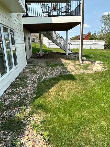 Backyard with a raised deck, stairs, and grass. A stone path is on the ground.