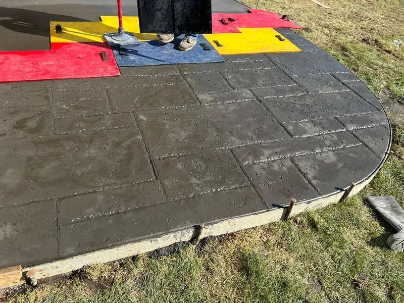 Wet concrete patio being stamped with pattern, person stamping it.