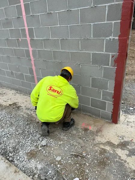 Construction worker inspecting a cinder block wall, wearing a yellow safety vest and helmet.