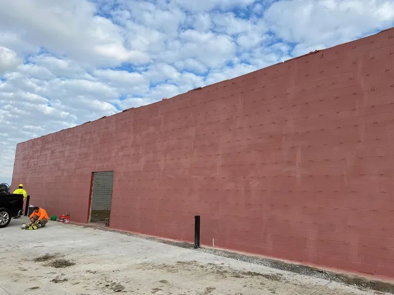 A long, red building with a small door; two workers by a truck on a cloudy day.