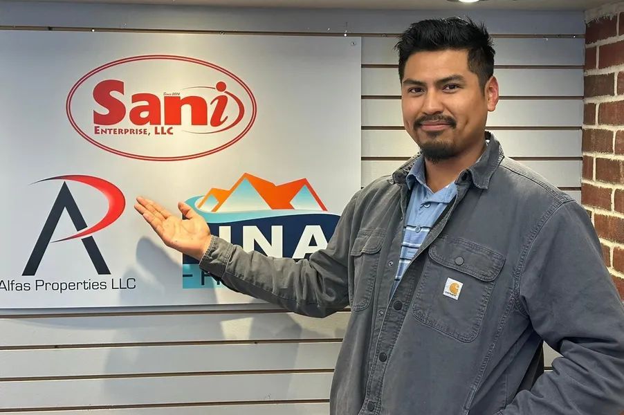 Man pointing to company logos on a wall: Sani Resources, Alpha Properties, and Fina Investments.