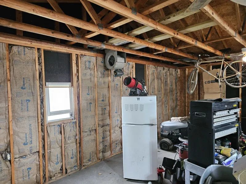 Garage interior with exposed insulation, window, refrigerator, tools, and a bicycle hanging from the ceiling.