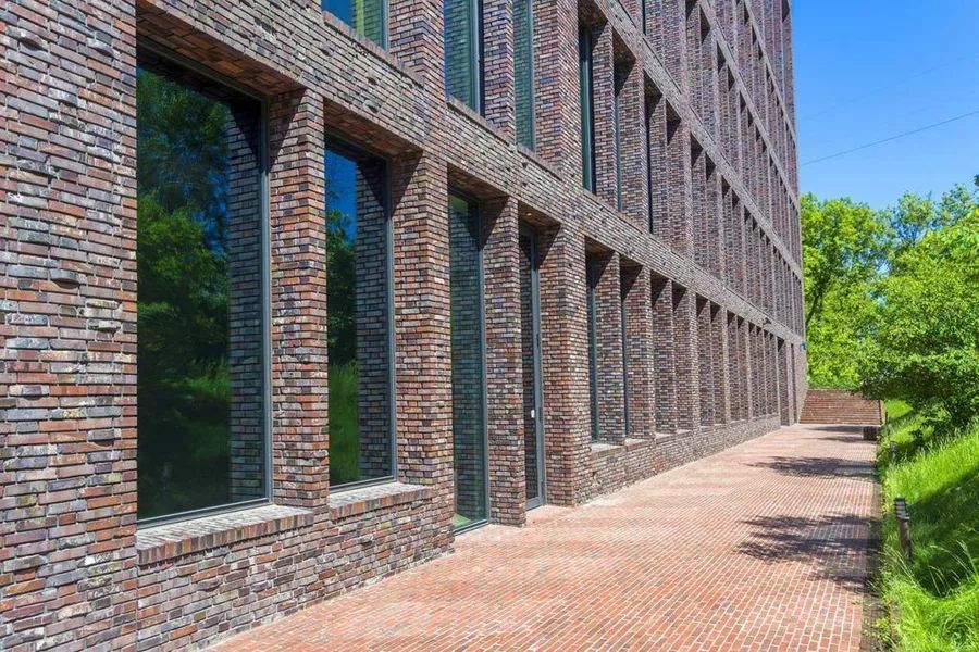 Brick building with tall windows and a brick walkway; bright sunlight.