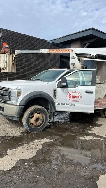 White work truck with extended arm lift by a building. The door is open.