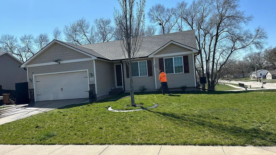House with gray siding and roof, green lawn, person in orange shirt, sunny day.