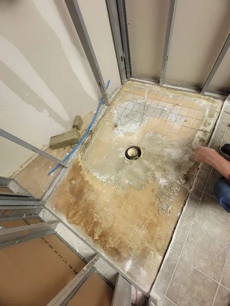 Shower construction in progress; exposed drain, concrete base, metal framing.