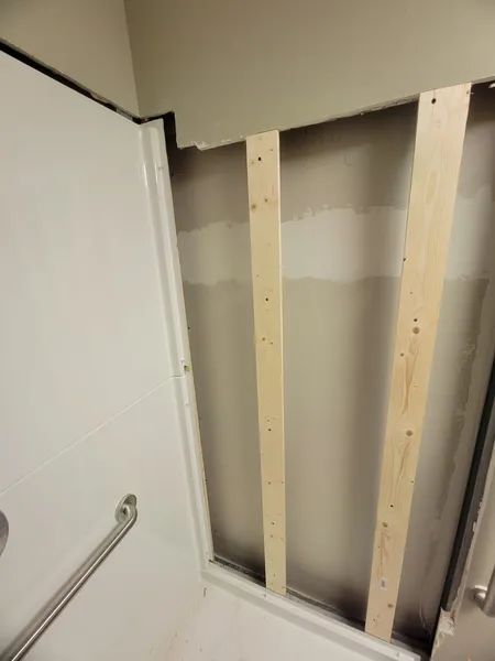 A bathroom shower stall with exposed wall studs and unfinished drywall.