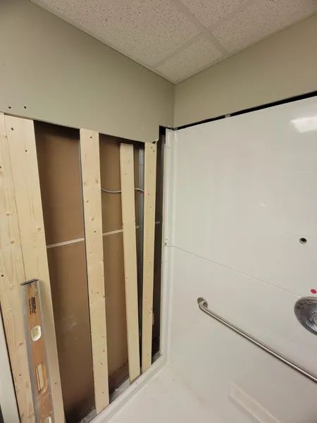 Framed wall opening next to a white shower enclosure. A level rests against the wooden frame.