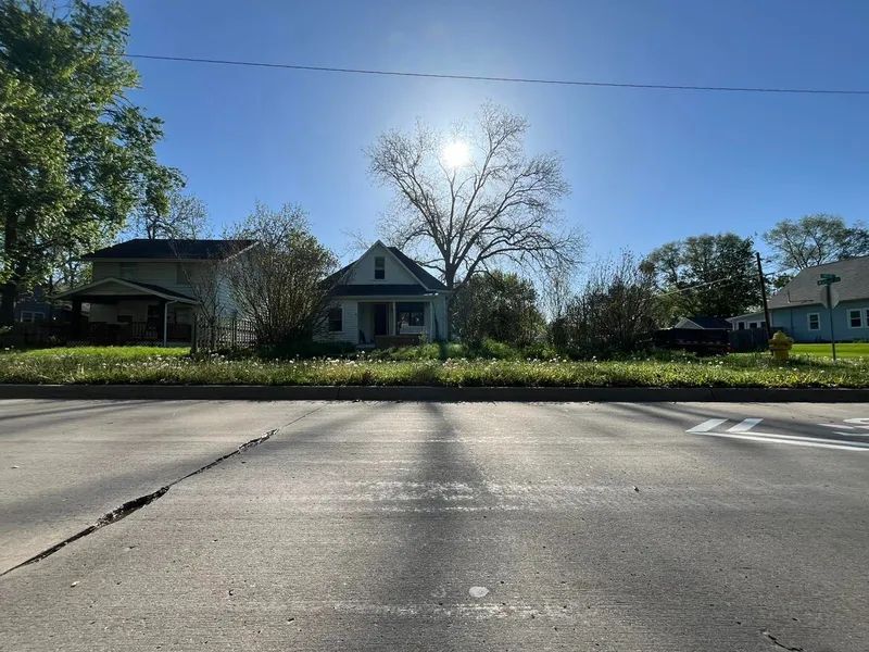 A house sits behind a road. The sun is overhead and partially obscured by a tree.