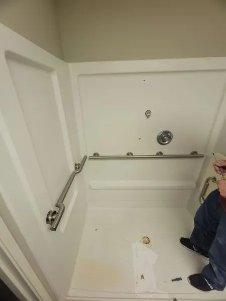 White accessible shower stall with grab bars and a person seated inside.