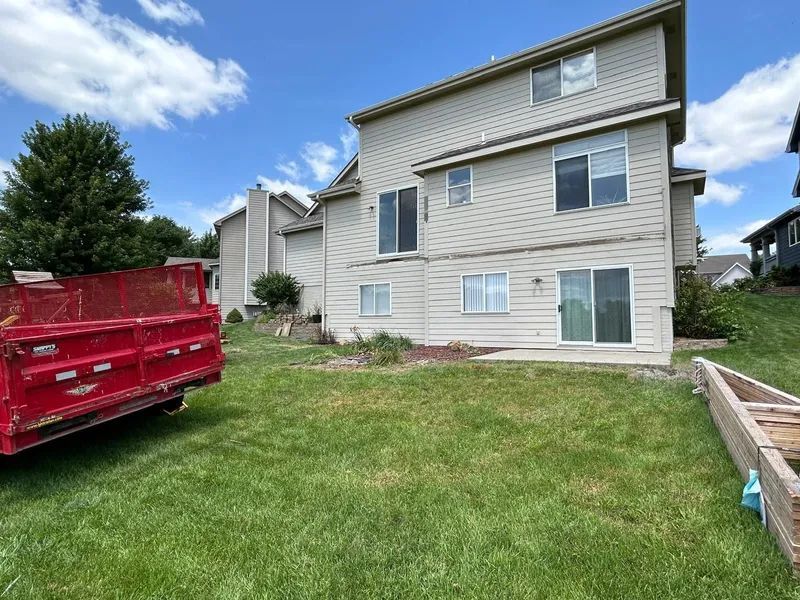 Backyard view of a two-story beige house with a red trailer and green grass.
