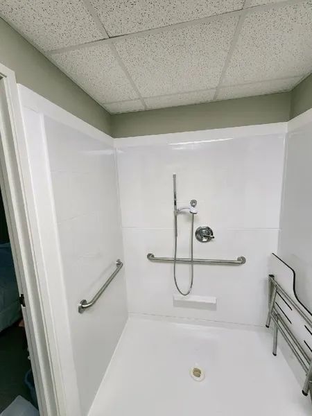 Accessible shower with grab bars and fold-down seat. White walls, chrome fixtures.