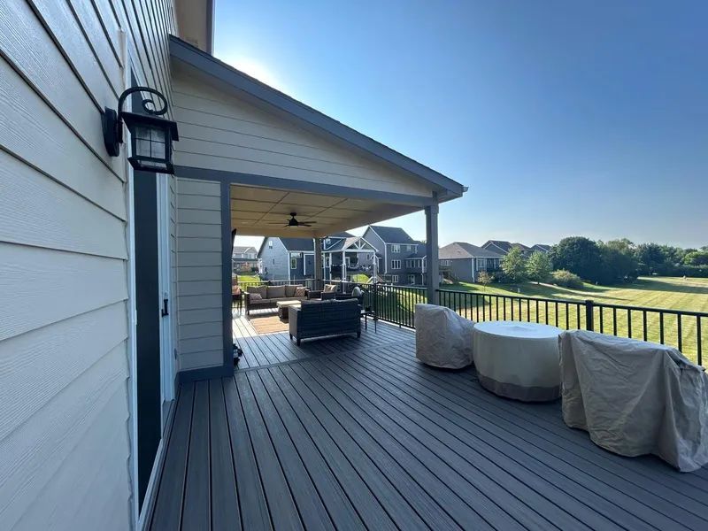 Grey deck with covered patio overlooking a grassy backyard; two covered chairs.