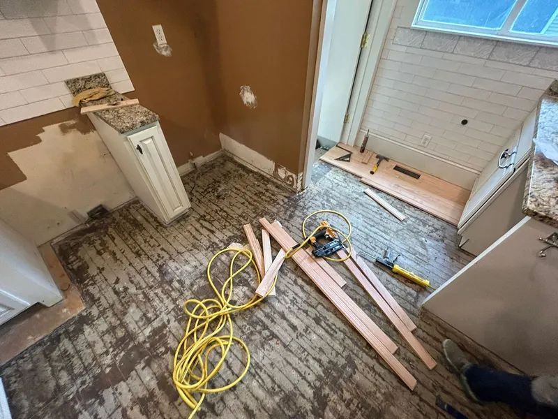 Kitchen renovation in progress: cabinetry, exposed subfloor, tools, wood trim pieces, and wall tile.