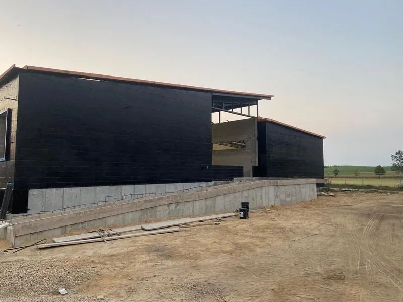 Black-sided building under construction with concrete ramp, set in a dry, outdoor environment.