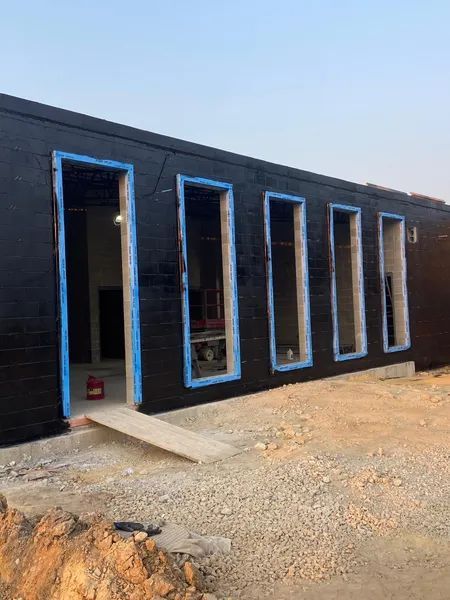 Black building exterior with window and door frames, blue tape, and a concrete ramp.
