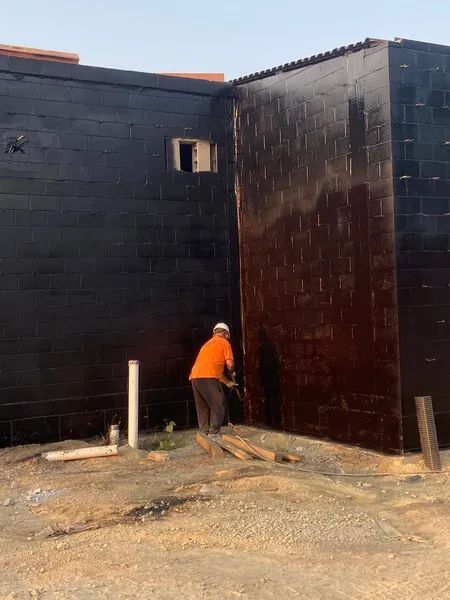 Man in orange shirt working on a dark, glossy brick wall; construction site.