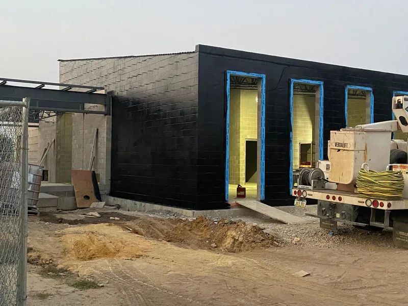 Exterior of a modern building under construction; black facade with three open doorways, adjacent ramp.
