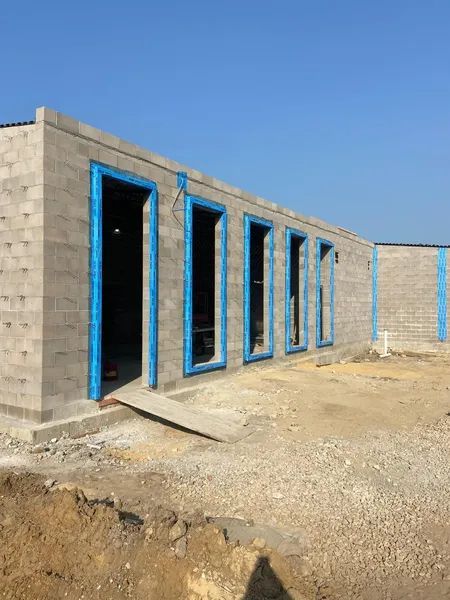 Exterior of a cinder block building under construction with blue frames around doorways and windows.