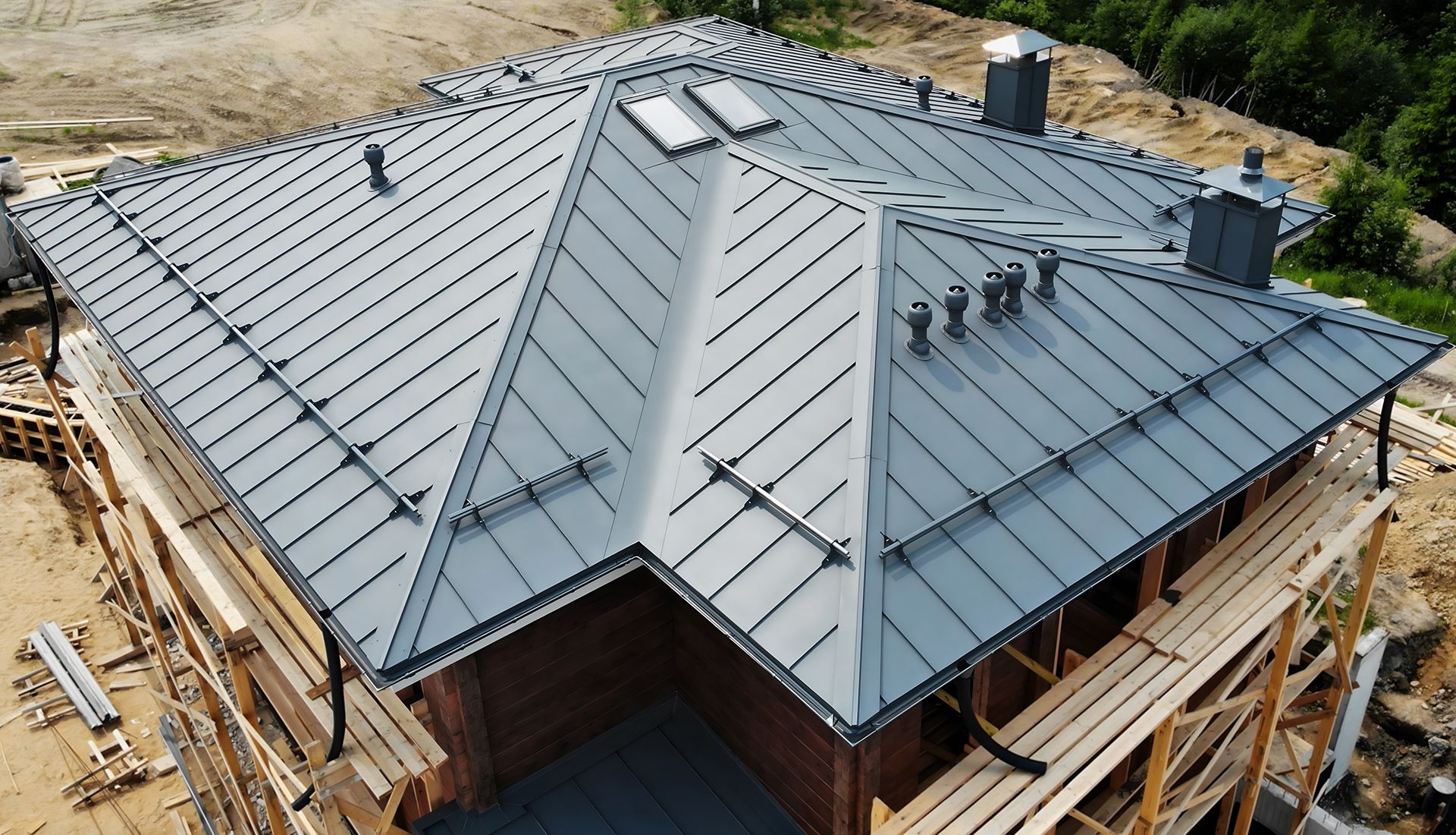 Newly constructed house with a gray metal roof, chimneys, and a construction site setting.
