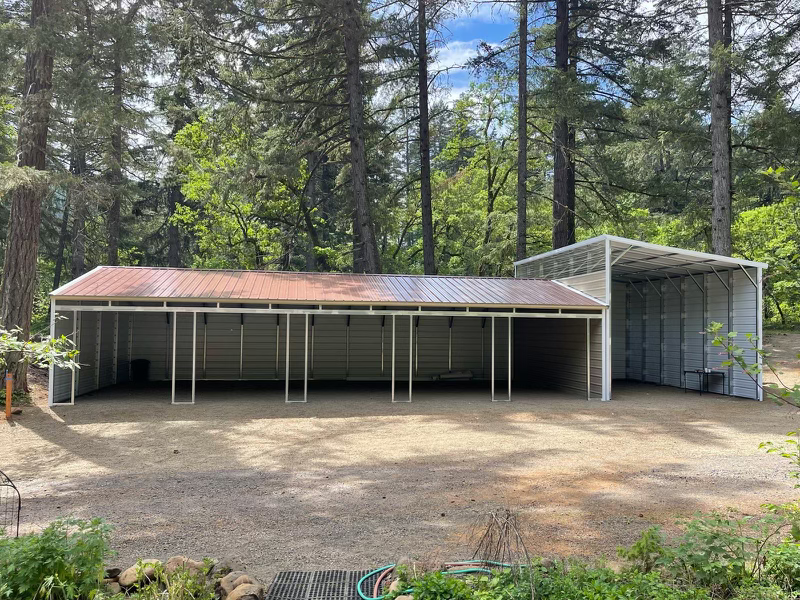 A large metal building with a roof in the middle of a forest.
