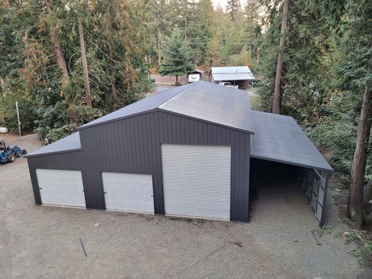 An aerial view of a large metal building with three garage doors surrounded by trees.