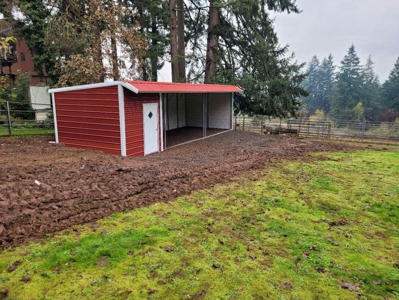 A carport is sitting in the middle of a gravel driveway surrounded by trees.